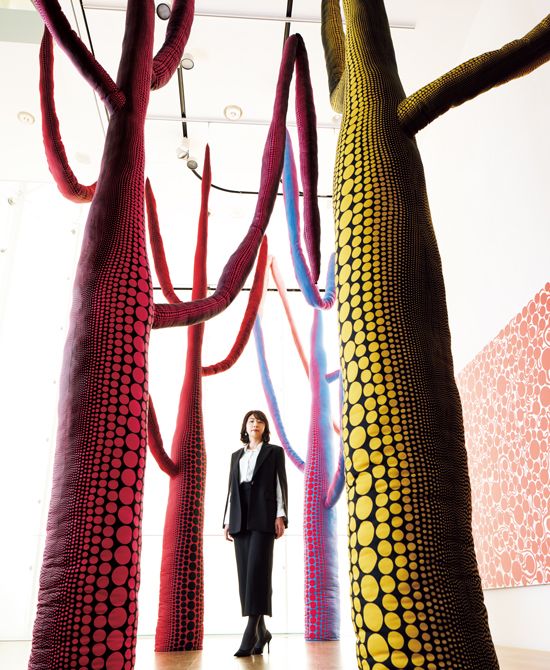 《再生の瞬間》(2024)どこかの星のまだ見ぬ森に迷い込んだような立体作品と九段さん。©YAYOI KUSAMA