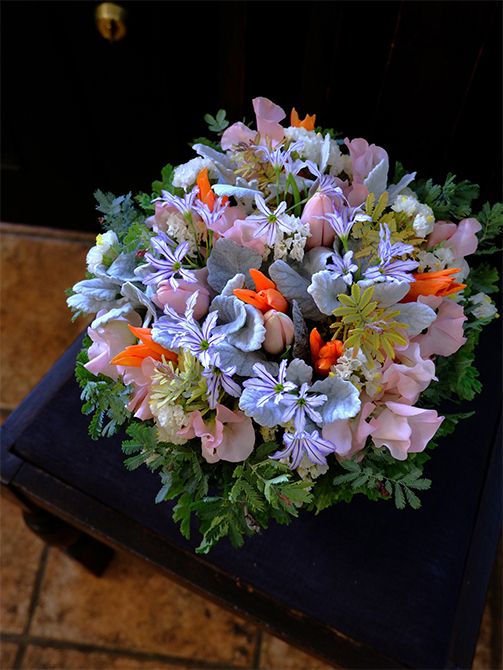 チューリップ‘バラードレディ’とスイートピー‘めぐみ’の優しいピンクに、リューココリーネ‘ジャパンブルー’を合わせた上品なアレンジです。スターチス‘シトロン’やダスティーミラーでパステルをボリュームアップし、オレンジ色のチューリップをアクセント使いに。金歯アカシア‘ツトム’をあしらいに加えました。退職される女性に感謝の贈り花です。