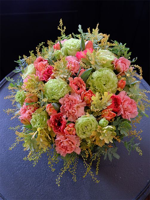 お義母さまの誕生日を祝う贈り花です。カーネーション‘ブリュレ’とラナンキュラス‘シャルロットオレンジ’。2種のアプリコット色をリシアンサス‘アンバーダブルモヒート’の黄緑糸対比させたアレンジです。ほかにチューリップ‘ロレンゾ’、アカシア‘オーレア’を使用。