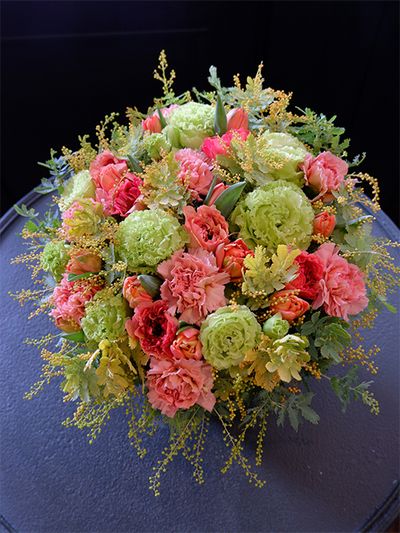 お義母さまの誕生日を祝う贈り花です。カーネーション‘ブリュレ’とラナンキュラス‘シャルロットオレンジ’。2種のアプリコット色をリシアンサス‘アンバーダブルモヒート’の黄緑糸対比させたアレンジです。ほかにチューリップ‘ロレンゾ’、アカシア‘オーレア’を使用。