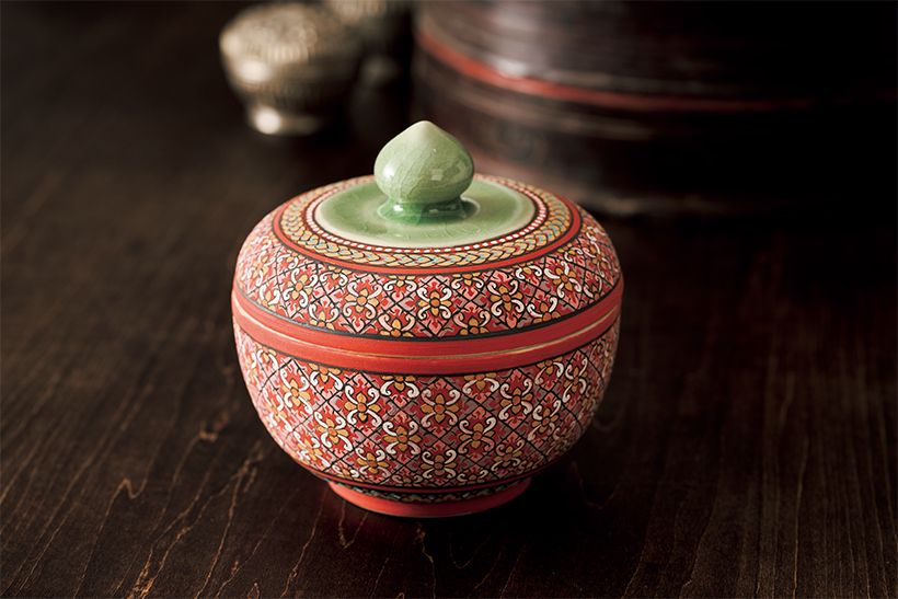 蓋のつまみの形は 蓮の花をモチーフ にしている。その 部分を除いた外側 には、赤を主体に した細密な文様が 絵付けされている。