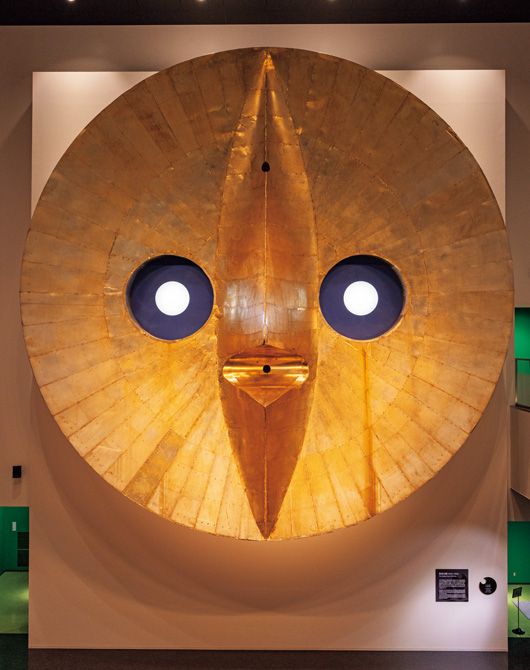 1970年開催の大阪万博の遺構を活用した記念館「EXPO’70 パビリオン」  大阪万博の貴重な資料や映像を展示する施設。パビリオンの一つであった「鉄鋼館」の建物が使われている。上・直径10.6㍍の初代「黄金の顔」。万博開催時には太陽の塔の頂点に設置されていた。2023年に増設した別館にて展示されている。下・会場でホステスが着用したユニフォーム。