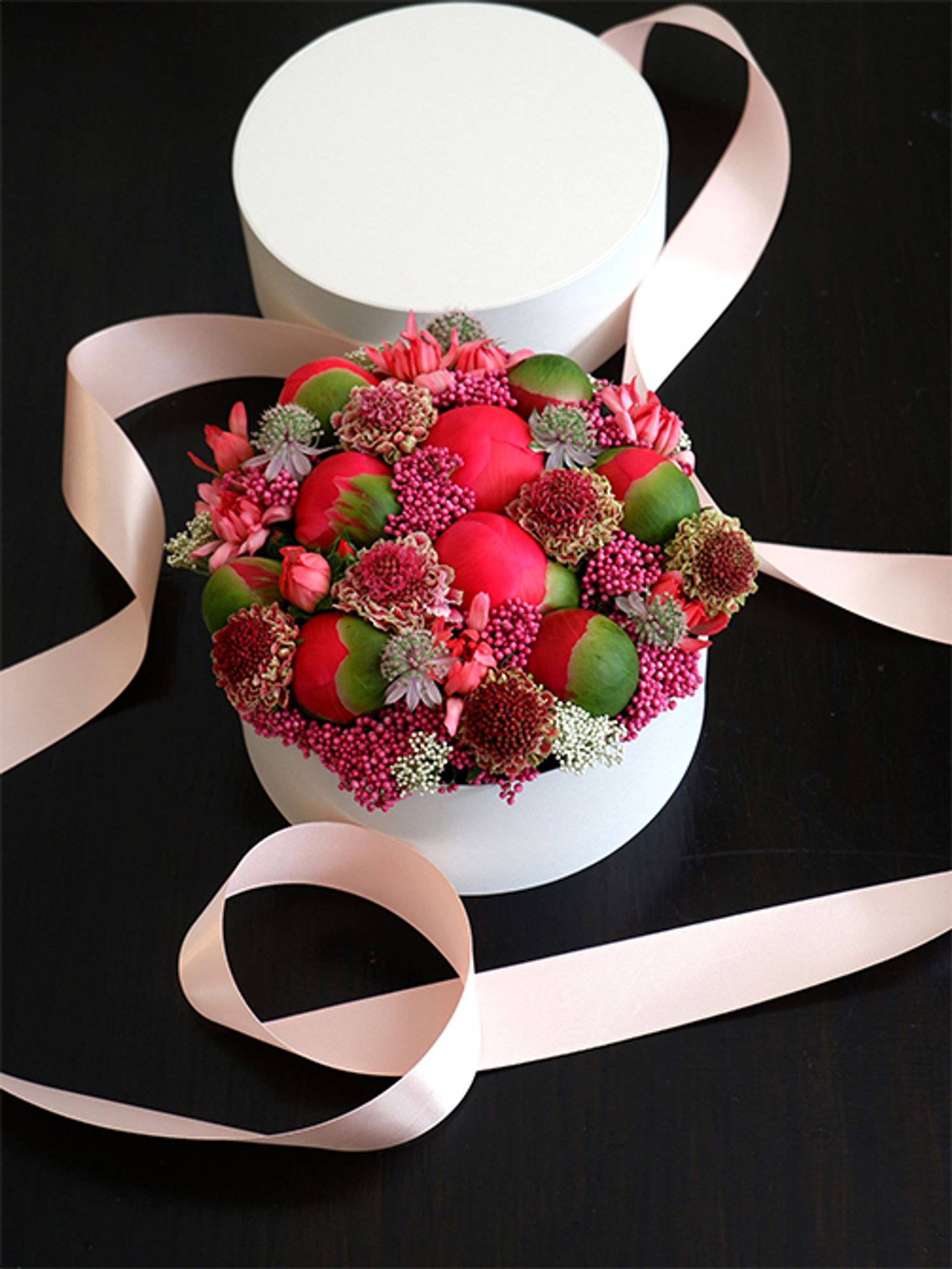 ライスフラワー‘マゼンタ’を使って、ボックスフラワーの贈り花を。ボール状の大きな蕾はシャクヤク‘コーラルチャーム’。スカビオサ‘コットンキャンディスクープ’も加え、すき間を埋めるようにライスフラワーやカーネーション‘ミニティアラ サーモン’、アストランティア‘フローレンス’を加えています。