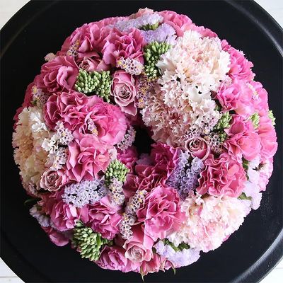 濃淡のピンクのカーネーションとバラを使い、メリハリのある表情に仕上げたリースです。淡いピンクは大輪カーネーション‘シャララ ピコ’。少しくすんだ濃いピンクのカーネーシヨンはスプレー咲きの‘モカスイート’。ほかにバラやスターチス、緑色のセダムなどを使っています。直径約20cmのフローラルフォームを使用。