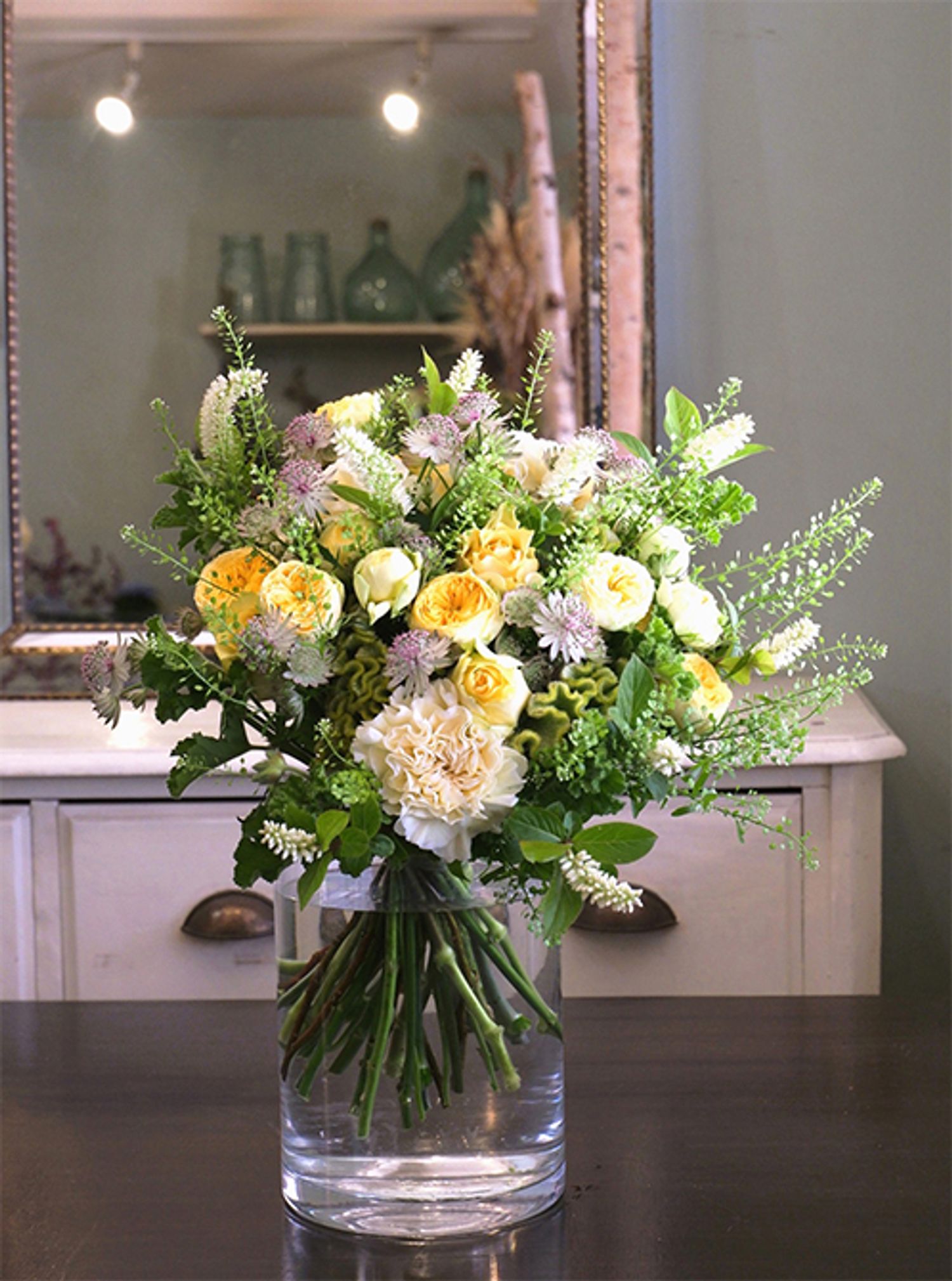 優しい黄色の中に、ほんのりピンクのアストランティアをアクセントに加えたブーケです。‘サニートレンドセッター’と‘スタニングムーン’の2種のバラ、カーネーション‘ポリミナミ’、ビターチョコゼラニウム、ヒメリョウブ‘心咲’を使用。ピンクの入り方がかわいらしいアストランティアは、ダイアナフラワーの富永さんから届いたものです。