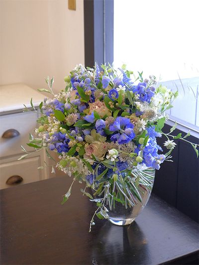 バラ‘ラピスヴェール’、アストランティア‘フローレンス’、セアノサス‘マリーサイモン’と、ごく淡いピンクの花に、デルフィニウム‘キュアノス’のブルーを合わせ、初夏の爽やかさが感じられるブーケを制作。ほかにシレネ‘小布施の郷’、ロシアンオリーブなどを使用。埼玉で暮らすお嫁さんへ、神戸のお義母さまからお礼の贈り花です。