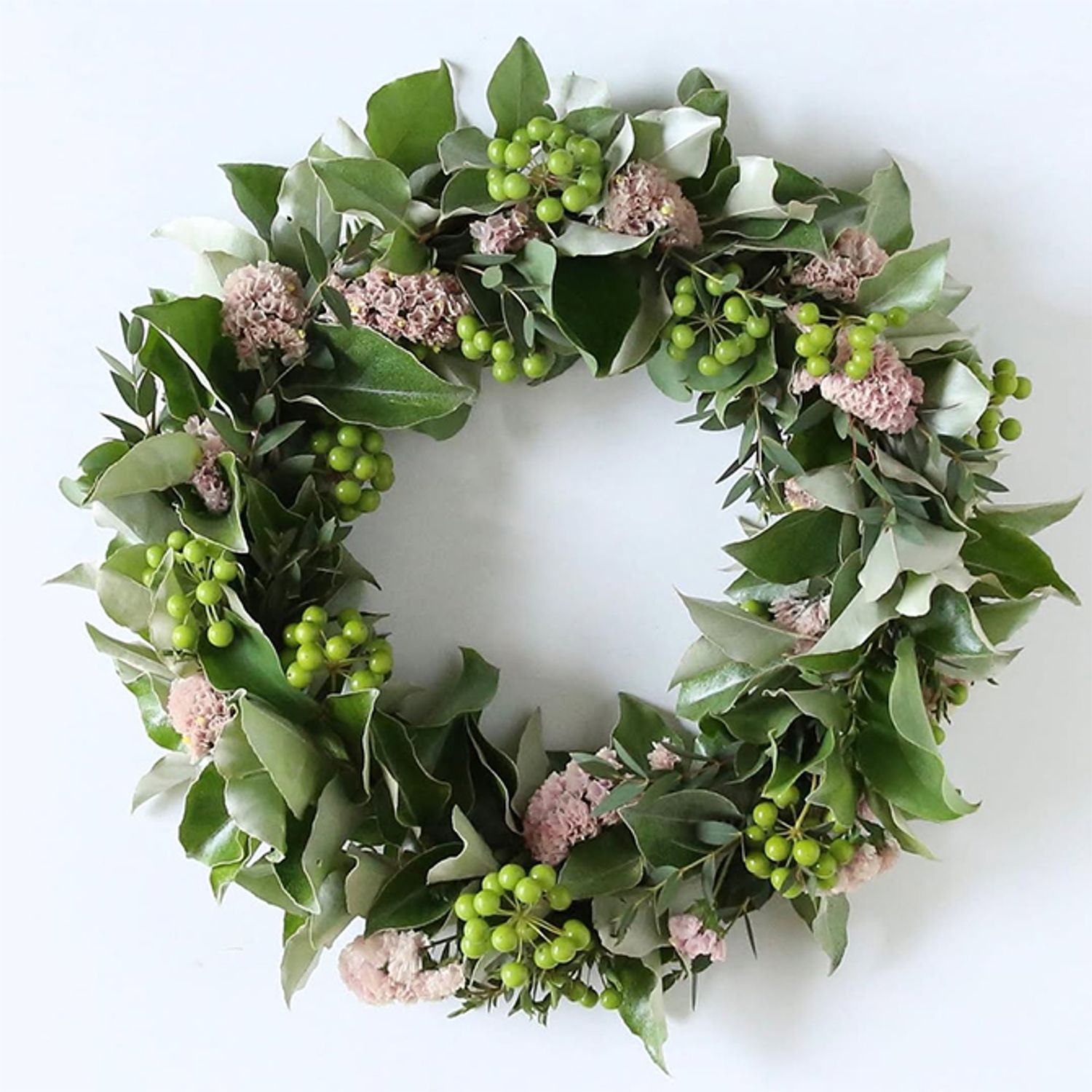 ワイヤーのリースベースを利用した緑のサンキライのフレッシュリースです。ほかに葉裏がシルバー色のギンバグミ、葉が小さなユーカリを使い、淡いピンクのスターチスをアクセントに加えています。いろいろな葉色に混じるサンキライの透明感ある実からフレッシュ感が伝わります。