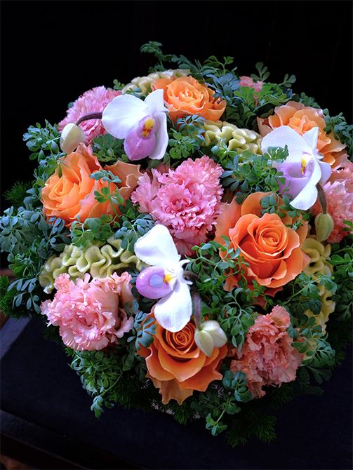息子さんご夫妻の結婚記念日に、ご両親からお祝いの贈り花です。リシアンサス‘セレブスパーク オレンジ’にあでやかなオレンジ色のバラ‘カルペディエム’を合わせ、シルバー色に近いケイトウ‘アスカセレクト スワプナ’、パフィオペディルム‘デレナティー’、ブルーリーフルーを加えたアレンジです。ブルーリーフルーの青みがかった葉色が、華やかなオレンジ色を引き立てます。