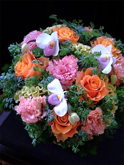 息子さんご夫妻の結婚記念日に、ご両親からお祝いの贈り花です。リシアンサス‘セレブスパーク オレンジ’にあでやかなオレンジ色のバラ‘カルペディエム’を合わせ、シルバー色に近いケイトウ‘アスカセレクト スワプナ’、パフィオペディルム‘デレナティー’、ブルーリーフルーを加えたアレンジです。ブルーリーフルーの青みがかった葉色が、華やかなオレンジ色を引き立てます。