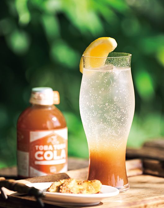 シロップは、コーラの語源「コラノキ」の実であるナッツから抽出したエキスも含む。シロップと炭酸水を1：4の割合で混ぜて飲む。合成着色料等は無添加。肥後さんが経営する奄美大島のリゾートホテル「ティダムーン」のショップで人気の「黒糖バナナ」を添えて。