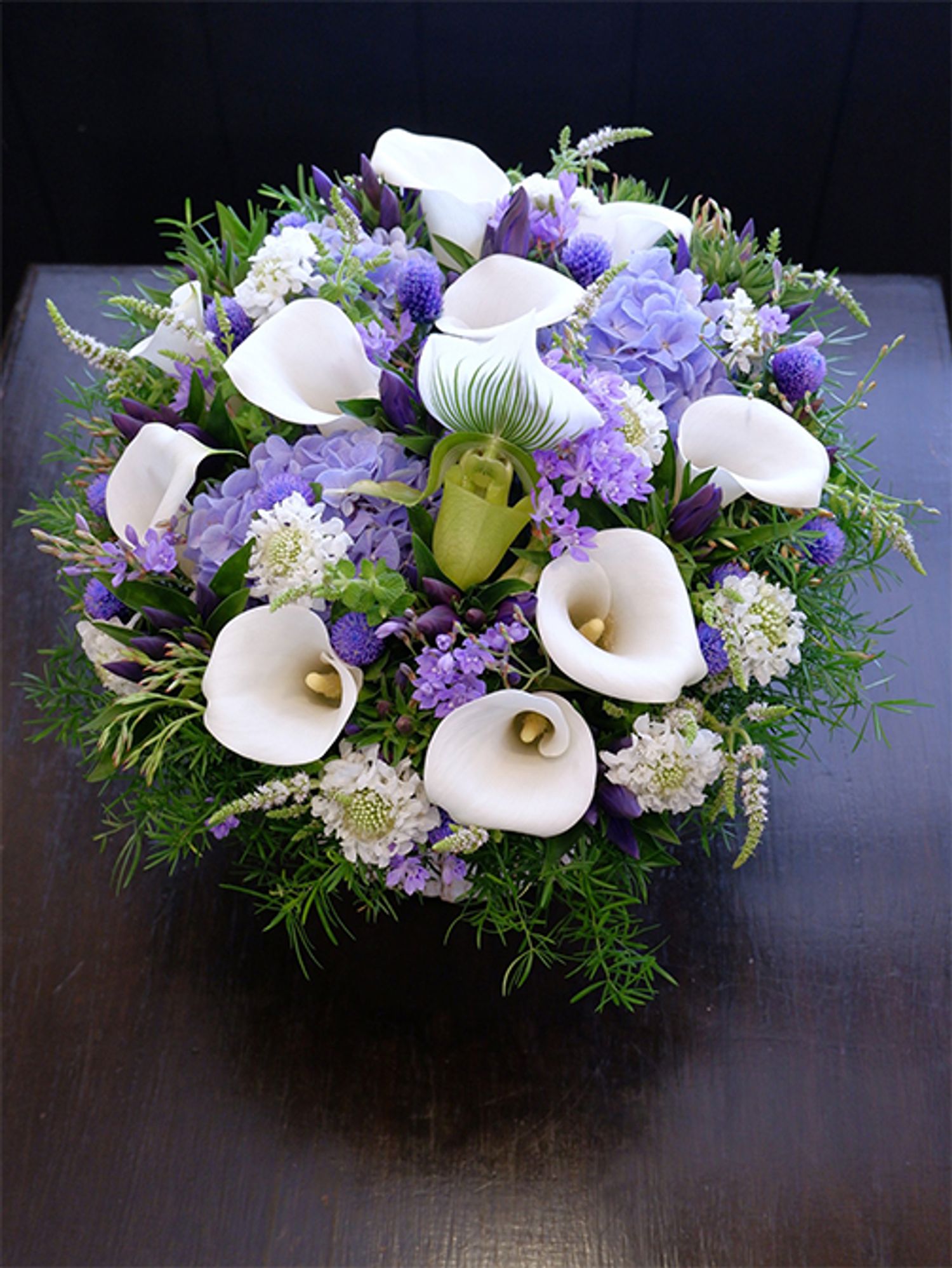 大阪の友人に夏の贈り花を。カラー‘サッポロ’とスカビオサ‘スクープ ホワイト’の白花にに、リンドウ‘FIブルー’、染めのセンニチコウ‘ブルー’、アジサイ‘アンティークブルー’、ラペイロージアの青花を合わせた涼しげなアレンジに。中心にパフィオペディルム‘クレアドルーン’を加えてアクセントにしました。「南原農園」さんのアスパラガス・スプレンゲリーとアップルミントをたっぷりあしらうと、よりクールでナチュラルな印象に。