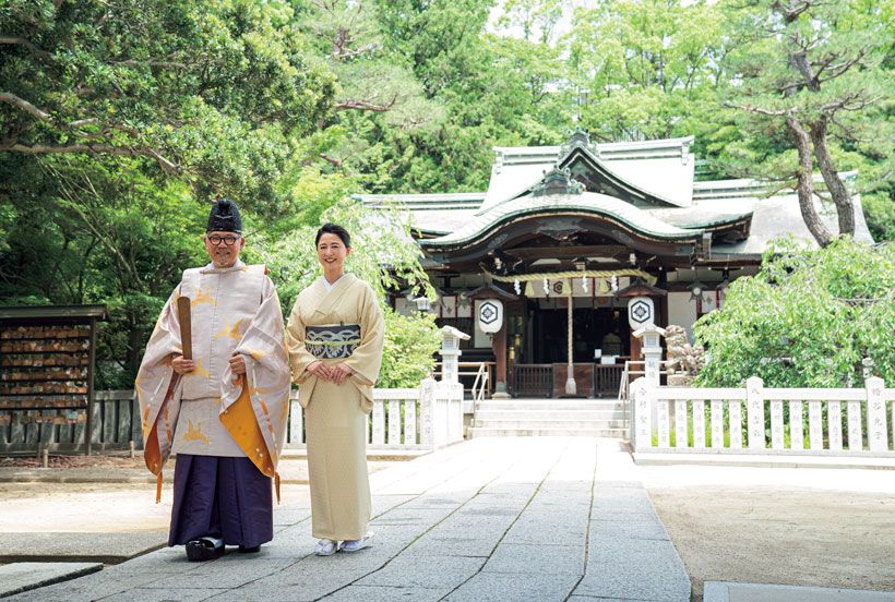 天穂日命（あめのほひのみこと）を御祭神とする芦屋神社は1100年以上の歴史を有する地元の守り神。御神木のヤマモモは樹齢300年以上。本殿の前で、宮司の山西康司さんと並ぶ妻で権禰宜の明子さん。