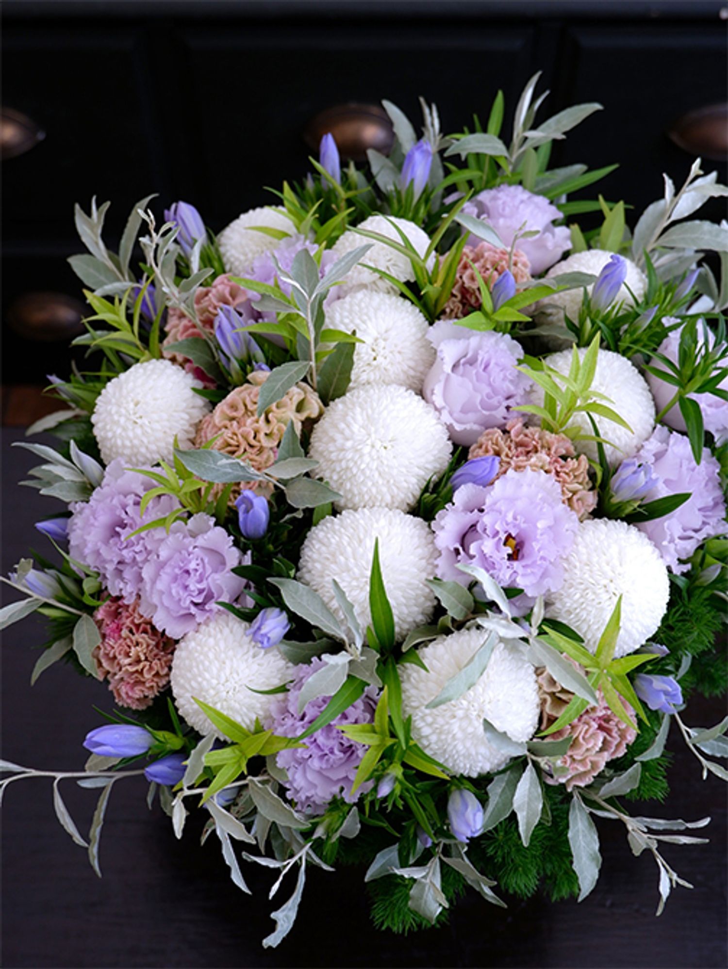 ボリューム感のあるまっ白なマムをメインに、ケイトウ‘プティフルーツ フェアリーローズ’やリシアンサス‘NFオトナラベンダー’など淡い花色を加えた涼やかなアレンジです。9月はまだまだ暑さが続くので、涼感のある贈り花も喜ばれます。アクセントに鮮やかなブルーのリンドウ‘ペールブルー’を加え、チョウジソウ、ロシアンオリーブなどのリーフをあしらいました。