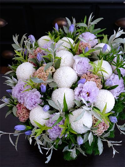 ボリューム感のあるまっ白なマムをメインに、ケイトウ‘プティフルーツ フェアリーローズ’やリシアンサス‘NFオトナラベンダー’など淡い花色を加えた涼やかなアレンジです。9月はまだまだ暑さが続くので、涼感のある贈り花も喜ばれます。アクセントに鮮やかなブルーのリンドウ‘ペールブルー’を加え、チョウジソウ、ロシアンオリーブなどのリーフをあしらいました。