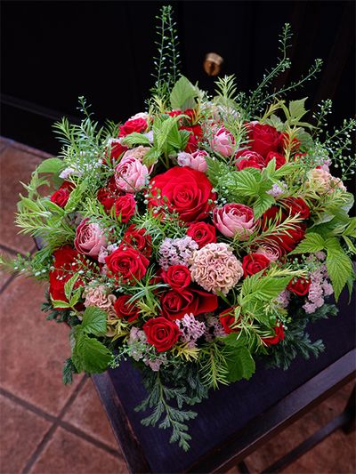 妹さんの還暦祝いに、お姉さんからの贈り花です。還暦（60歳）といえば、テーマカラーは赤ということで、鮮やかな赤バラ‘ブリランテ’をメインにしたアレンジを制作しました。あでやかなピンクのバラ‘チアフル’、ページュがかったピンクのケイトウ‘プティフルーツ フェアリーローズ’、透明感のあるピンクのスターチス‘ソロモン’と、ニュアンスが異なるピンクを脇役として利用しました。ほかにバラ‘レディーラブ’、メラレウカ‘レボリューションゴールド’、コニファー‘ブールヴァール’、フランボワーズなどを使用。