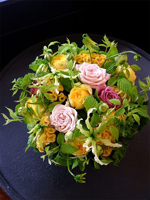 ケイトウ‘アスカセレクト ひよこ’と蕾つきバラ‘カタリナ’は一つ前の贈り花と同じですが、ブルーの花ではなく、濃淡ピンクのバラと合わせるとぐっとエレガントな印象に。淡いピンクのバラは‘ウエストミンスターアビー’、シックな濃いピンクのバラは‘アヴニール＋’。ほかにグロリオサ‘ツルヒメ’、グリーンワッフルゼラニウム、フランボワーズなどを使用。