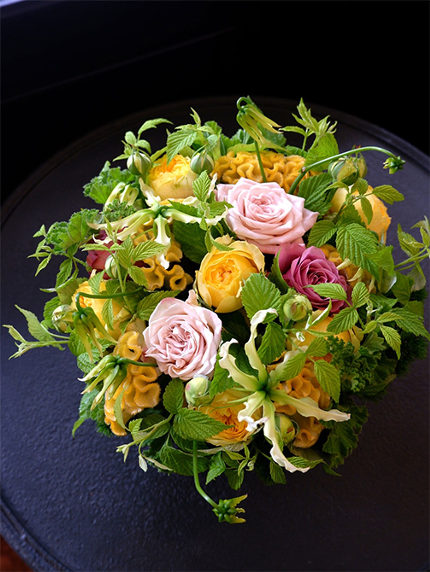 ケイトウ‘アスカセレクト ひよこ’と蕾つきバラ‘カタリナ’は一つ前の贈り花と同じですが、ブルーの花ではなく、濃淡ピンクのバラと合わせるとぐっとエレガントな印象に。淡いピンクのバラは‘ウエストミンスターアビー’、シックな濃いピンクのバラは‘アヴニール＋’。ほかにグロリオサ‘ツルヒメ’、グリーンワッフルゼラニウム、フランボワーズなどを使用。