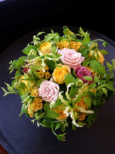 ケイトウ‘アスカセレクト ひよこ’と蕾つきバラ‘カタリナ’は一つ前の贈り花と同じですが、ブルーの花ではなく、濃淡ピンクのバラと合わせるとぐっとエレガントな印象に。淡いピンクのバラは‘ウエストミンスターアビー’、シックな濃いピンクのバラは‘アヴニール＋’。ほかにグロリオサ‘ツルヒメ’、グリーンワッフルゼラニウム、フランボワーズなどを使用。