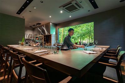 庭に面した大きな窓から光が差し込むレストラン棟。厨房を囲むL字型のカウンター席から、シェフ達の仕事を間近に楽しめる。