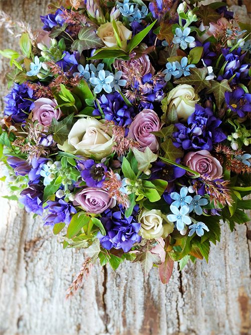 花屋さんのお母様へ誕生日の贈り花という依頼を受け、シックな花色にブルーを加えたアレンジを制作しました。ブルーの花は、オキシペタルム‘ピュアブルー’、リンドウの‘モダンブルー’と‘深山ラブ’。バラは‘デザート’と‘ライラッククラシック’。ルビーグラスや染めのアップライトアイビー、ヒペリカム‘マジカルレッド’、紅葉ヒペリカムなどを加えて秋の雰囲気たっぷりに仕上げました。