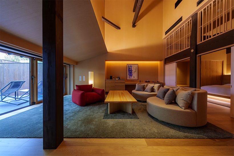 「凪」の客室。モダンな家具が配された、天井の高いリビングルーム。奥にベッドルームがある。露天風呂は石造り。