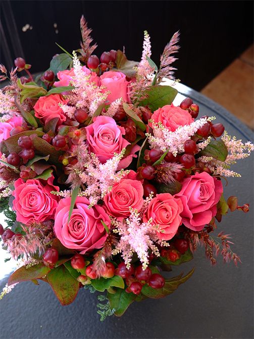 お孫さんの誕生日を祝う贈り花です。あでやかなピンクのバラ‘オール4ラブ＋’とアスチルベ‘ライトピンク’、濃淡のピンクを引き立て、秋らしい雰囲気をもたらしているのが鮮やかに紅葉したヒペリカム‘マジカルシーズンズ’です。淡いピンクに色づく穂が繊細で美しいルビーグラスも加え、季節感たっぷりのアレンジに。