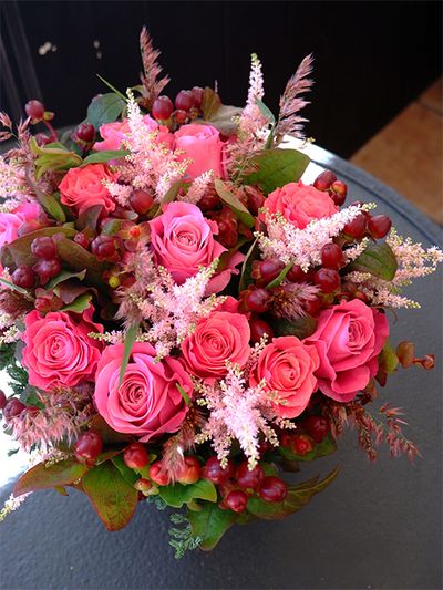お孫さんの誕生日を祝う贈り花です。あでやかなピンクのバラ‘オール4ラブ＋’とアスチルベ‘ライトピンク’、濃淡のピンクを引き立て、秋らしい雰囲気をもたらしているのが鮮やかに紅葉したヒペリカム‘マジカルシーズンズ’です。淡いピンクに色づく穂が繊細で美しいルビーグラスも加え、季節感たっぷりのアレンジに。