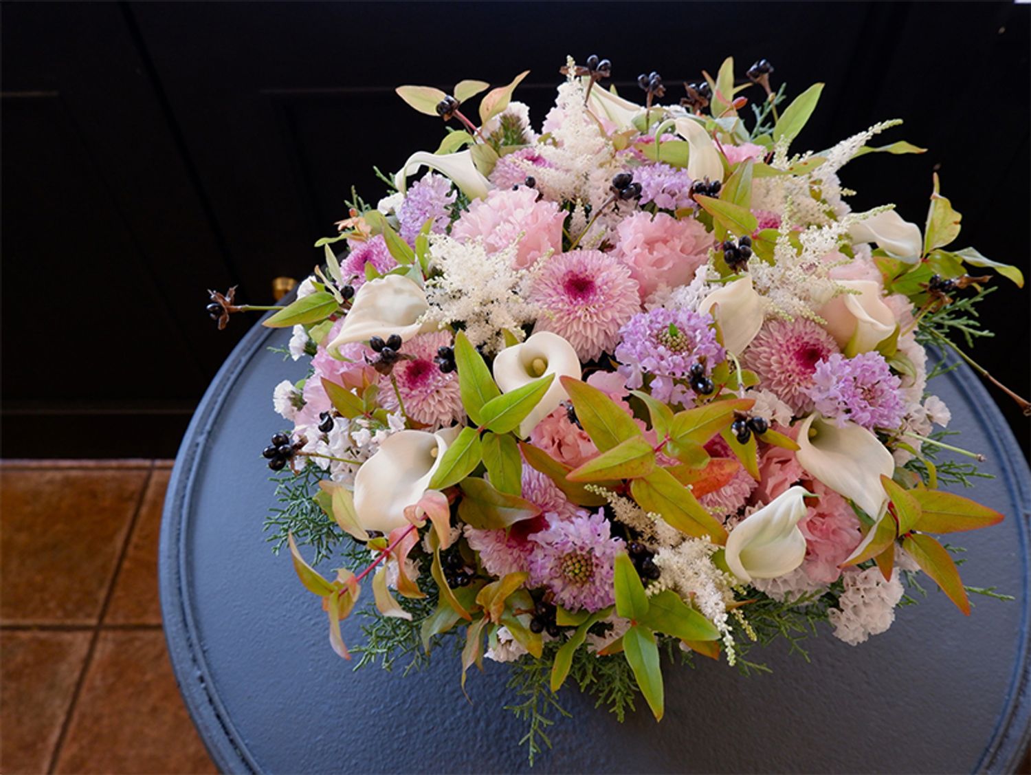 秋らしさを感じさせるマムの贈り花をもう1点。立体感のあるポンポン咲きのマム‘アビー’を使い、淡いパステル系の花色合わせにしてみました。ピンクのリシアンサスは‘ボヤージュ チャームピンク’。やや紫がかったピンクのスカビオサは‘テラ239’。白い花はカラー‘キャプテン ベンチュラ’とアスチルベ‘ダイヤモンド’、スターチス‘パルク’。原種系紅葉ヒペリカムやシロヤマブキの実で秋の雰囲気を加えました。深みのある花色が多い中、軽快なパステルカラーが新鮮な印象です。