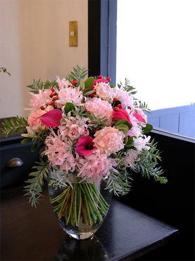 お客様を迎える室内に飾る花を、というオーダーをいただき、淡いピンクのダイヤモンドリリーとリシアンサス‘ボヤージュ ピンクシェイク’を使ったブーケを制作しました。アクセントに加えたのは濃いピンクのカラー‘トーキョー’。ちらちらと見える赤い実はこの時期に出回るローズヒップ‘アメージングファンタジー’です。淡いピンクにあわせ、シルバーリーフのアカシア‘ブルーブッシュ’とフェイジョアをあしらって、全体を優しいトーンにまとめました。