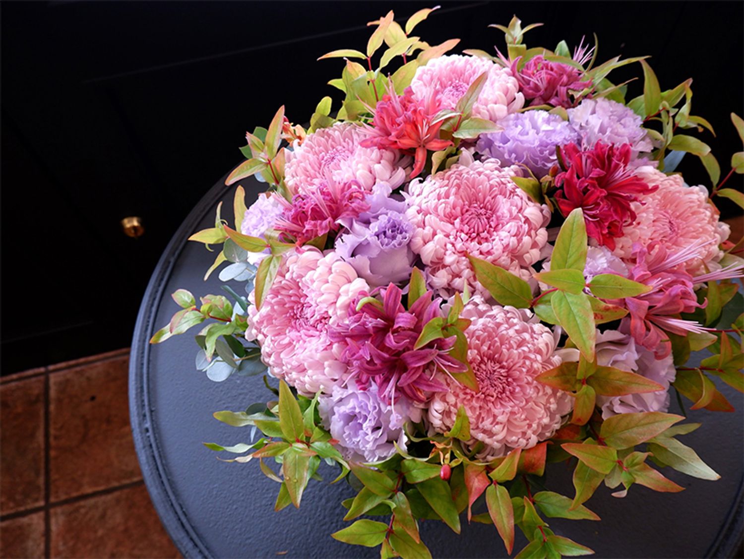 デコラ咲きのマム‘ララバイ’と「横山園芸」さんのダイヤモンドリリーの花合わせで、誕生日を祝う贈り花を制作。透明感のある薄紫のリシアンサス‘NFオトナラベンダー’をアクセントに加えると、上品で大人っぽいピンクアレンジに。原種系の紅葉ヒペリカムが季節感をもたらしてくれます。