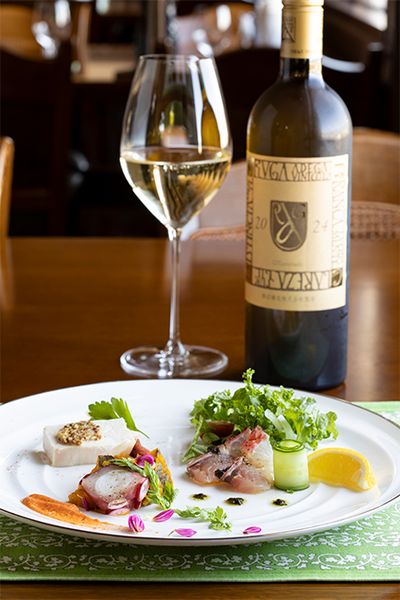 「前菜盛り合わせ」（2750円）とキリっとしたクリアーな味わいが特徴の「アルガブランカ クラレーザ 2024」。前菜は、右から時計回りに、オナガダイのカルパッチョ、たこのボイル、信玄鶏の低温調理。野菜からエディブルフラワーに至るまで、地元の生産者から新鮮なものを仕入れている。