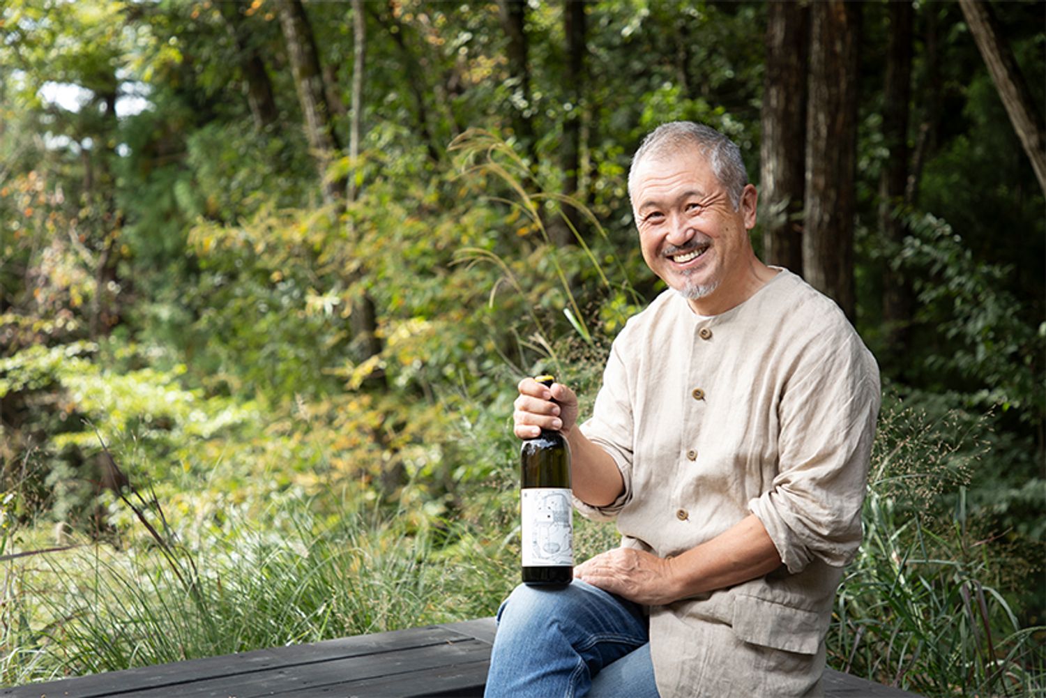 「98WINEs」代表の平山繁之さん。手にするのは「芒（NOGI）」2024の白（3850円）。「自分の造るワインの中に、“一番おすすめ”や“一番好き”などといった優劣はない。場所の違い、ぶどうの品種の違いが、異なる味わいのワインを造り出す、ただそれだけです」。
