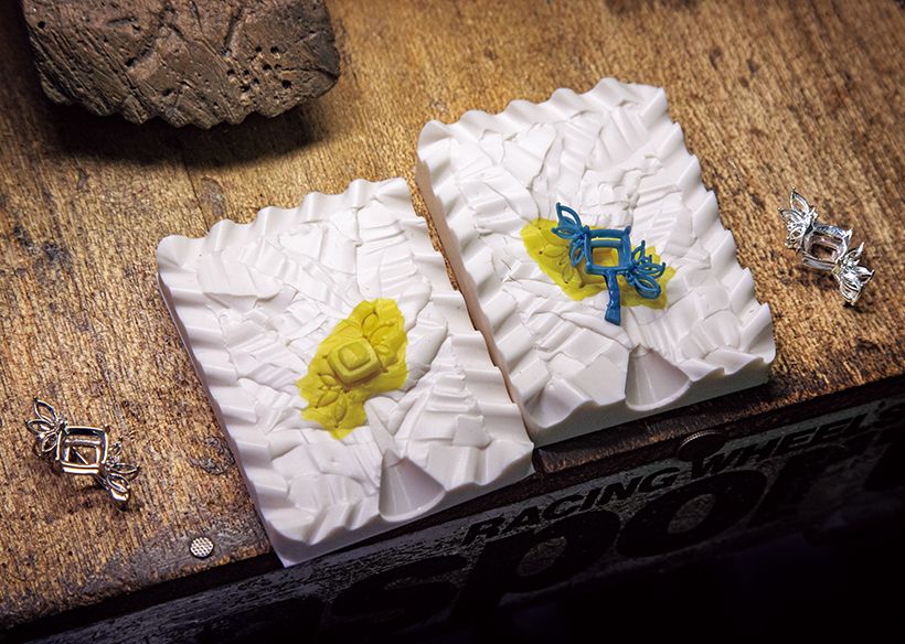 2.ブローチの金属部分の制作工程。シルバーで成形した原型（写真左端）から作った黄色いシリコンゴムの型を用いて青いワックス型を作製。石膏に入れて熱を加え、ワックスが溶け出した後にできた空洞にプラチナを流し込む。右端が完成品。