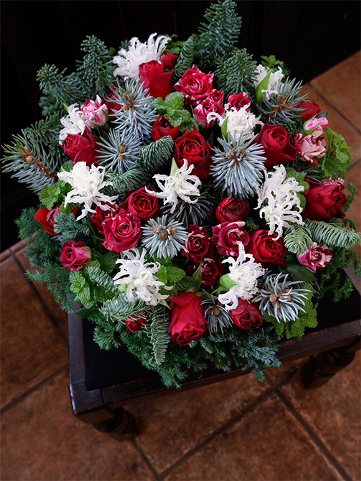 赤バラの‘ブリランテ’と赤×白の‘フリューレット’に、純白のクリスパリリーを合わせたアレンジ。繊細な花形のクリスパリリーは、枝に積もった雪のようにも見え、ホワイトクリスマスをイメージさせます。ほかに赤いラナンキュラスの‘パミエ’、ブンゲンストウヒ‘ホプシー’、スペアミントなどを使用。コニファー類を加えると一気にクリスマス感が増します。