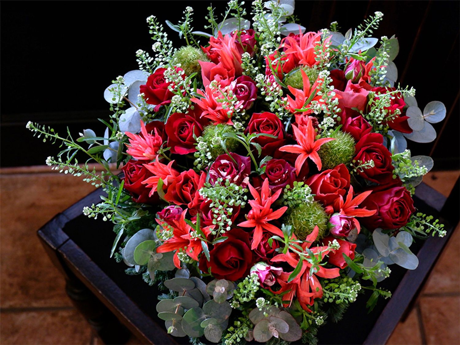 赤バラの‘ブリランテ’と‘フリューレット’の組み合わせですが、朱赤のダイヤモンドリリー‘スカーレット’を加えると、より赤が印象的に。花色が強くなりすぎないよう、緑のガーベラ‘みころん’、タラスピオファリムの優しいグリーンとシルバーリーフのユーカリで調和しています。