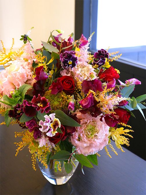 お部屋に飾る花束をというオーダーをいただき、スイートピー‘ショコラ’にバラやパンジーなど、シックな赤系の花を合わせると、大人っぽい雰囲気に。淡いピンクのリシアンサスや金葉アカシア‘ツトム’を加えて軽やかな印象に仕上げました。バラは‘ブリランテ’、パンジーは‘ミッドナイトムーン’、リシアンサスは‘NFアッシュ’、‘ボヤージュピンク’、‘エグゼアンティークピンク’の3種を使用。アスチルベ‘ライトピンク’の軽やかな穂花も加えています。