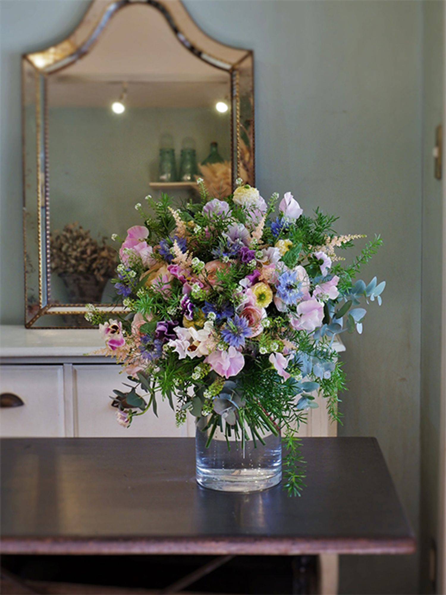 ‘ペッシュ’の淡いピンクに、ラナンキュラスやパンジー、アスチルベなど春のパステルカラーを合わせたブーケを誕生日の贈り花に。ニゲラ‘ミスジーキル’の水色が加わるとぐっと大人っぽくエレガントな印象になります。ラナンキュラスの‘リナレモン’と‘オルレアン’、パンジー‘カルメン’、アスチルベ‘アプリコット’などを使用。アスパラガス・スプレンゲリーなどのリーフをたっぷり加えてナチュラルな印象に仕上げました。