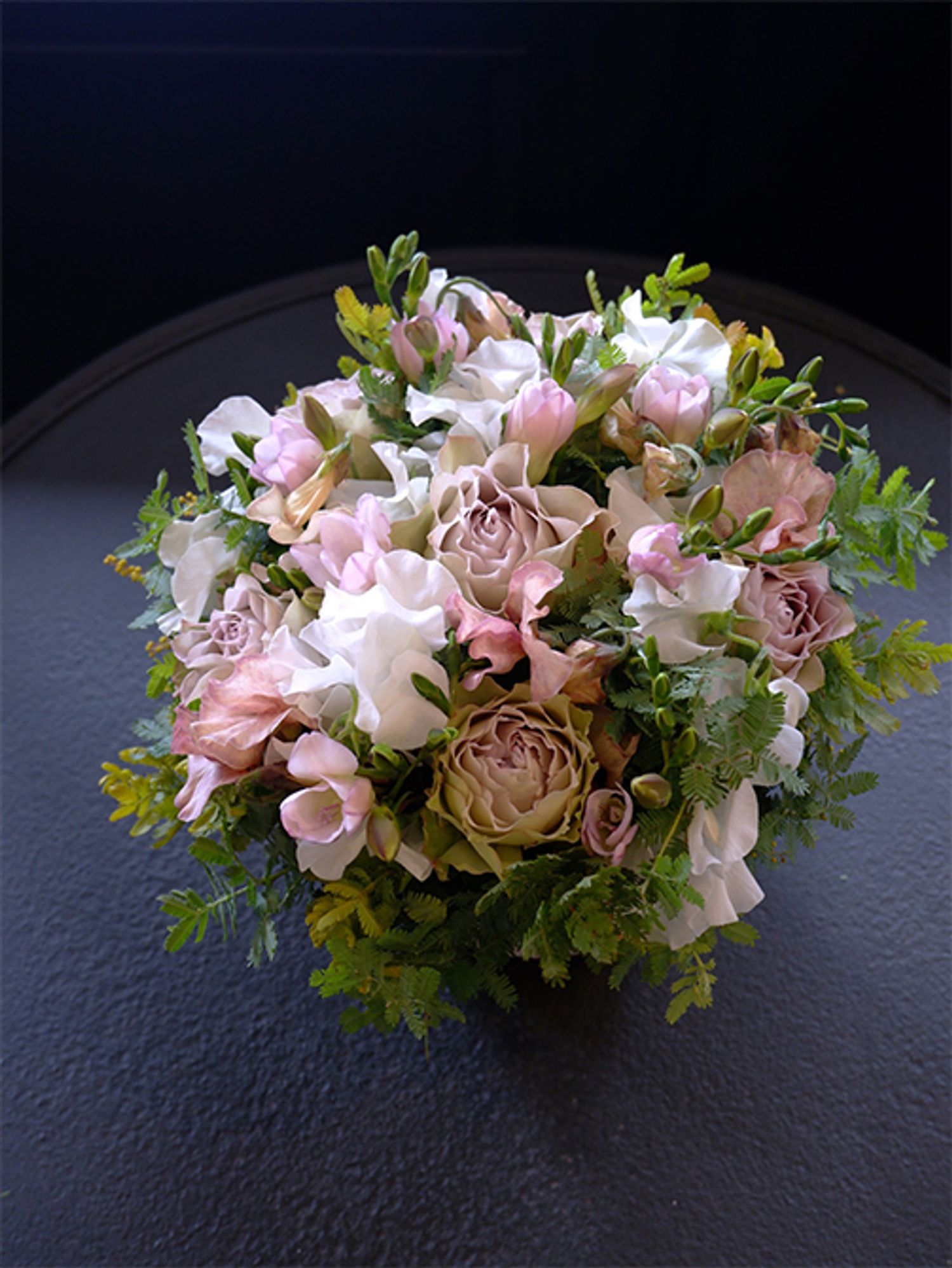 染めのスイートピー‘メロウ’とくすみ系の花色が魅力的なバラ‘ラピスヴェール’。アンテク感のある花色の2種を合わせると、落ち着いた雰囲気の上品な贈り花に。純白のスイートピー‘ロイヤルホワイト’を加えると、くすみ系の花色がより際だって見えます。ほかにフリージア‘エアリーシェルピンク’、銀葉アカシアを使用。いつもおしやれな友人の誕生日を祝うアレンジです。