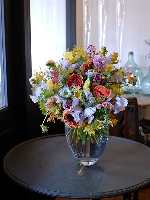 染めのスイートピー‘アッシュブルー’を利用した春のエレガントなブーケを誕生日の贈り花に。水色と淡いクリーム色の優しい色合いに、アクセントとしてラナンキュラス‘シャルロットオレンジ’を加えました。ほかにパンジー‘カルメン’、ニゲラ‘ミスジーキル’、金葉アカシア‘ツトム’などを利用しています。