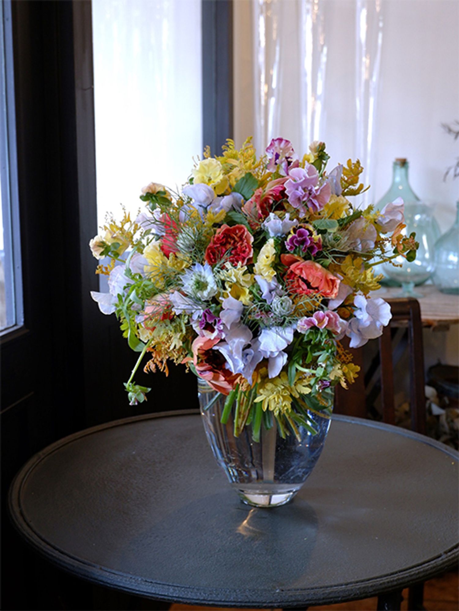 染めのスイートピー‘アッシュブルー’を利用した春のエレガントなブーケを誕生日の贈り花に。水色と淡いクリーム色の優しい色合いに、アクセントとしてラナンキュラス‘シャルロットオレンジ’を加えました。ほかにパンジー‘カルメン’、ニゲラ‘ミスジーキル’、金葉アカシア‘ツトム’などを利用しています。