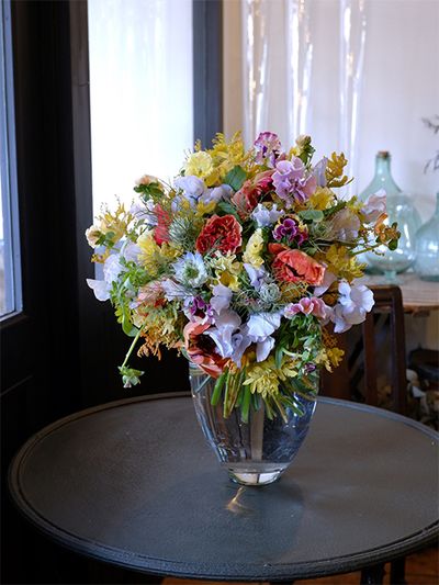 染めのスイートピー‘アッシュブルー’を利用した春のエレガントなブーケを誕生日の贈り花に。水色と淡いクリーム色の優しい色合いに、アクセントとしてラナンキュラス‘シャルロットオレンジ’を加えました。ほかにパンジー‘カルメン’、ニゲラ‘ミスジーキル’、金葉アカシア‘ツトム’などを利用しています。