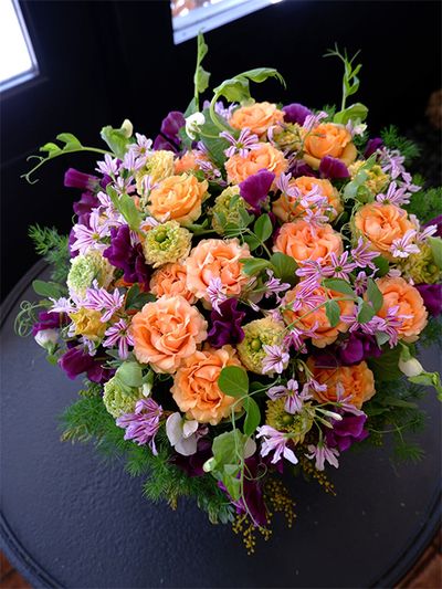 枝付きスイートピー‘夜間飛行’に淡いオレンジ色のバラ‘玉かずら’を合わせると、色の対比からより立体感のあるアレンジに。ほかにラナンキュラス‘リナレモン’、リューココリーネ‘ストライプピンク’を使用。エンドウマメも加え、つるの動きが楽しい雰囲気を出しています。誕生日の贈り花です。