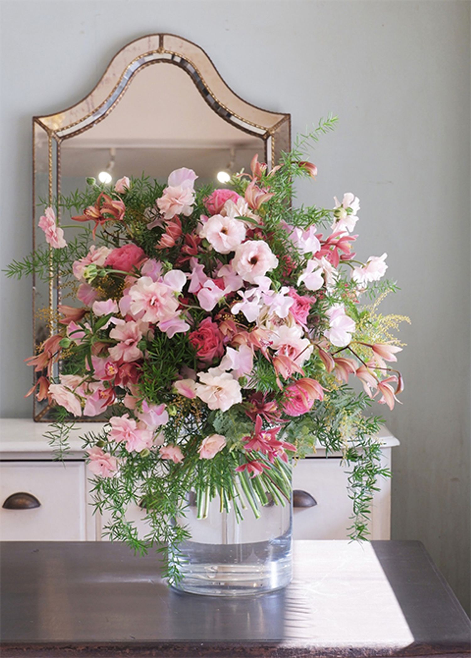 「ファームたかお」さんのオリジナルスイートピー‘ペッシュ’を使い、お姉さんの古希を祝う妹さんからの贈り花を制作しました。‘ラックス アリアドネ’、‘あけぼの’、‘オルレアン’の3種のラナンキュラスに、シンビジウムの‘桐壺’と‘情熱’を合わせ、アスパラガス・スプレンゲリーをあしらったブーケです。モモのような淡いピンクのスイートピーが、蝶が舞うように軽やか。