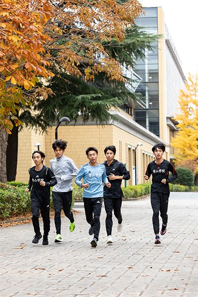 青山学院大学相模原キャンパスの構内でジョグをする4年生たち。左から、黒田主将、佐藤有一選手、荒巻選手、宇田川選手、神田大地副主将。荒巻選手と神田副主将は選手としての出場はならなかったが、荒巻選手は8区塩出選手の給水係を、神田副主将は3区宇田川選手の給水係を務め、同期に力を与えた。ちなみに寮母の美穂さんは「今年の4年生はゴーイングマイウェイな感じだけど、宇田川くんと神田くんはいつも一緒にいるかな」と話していた。