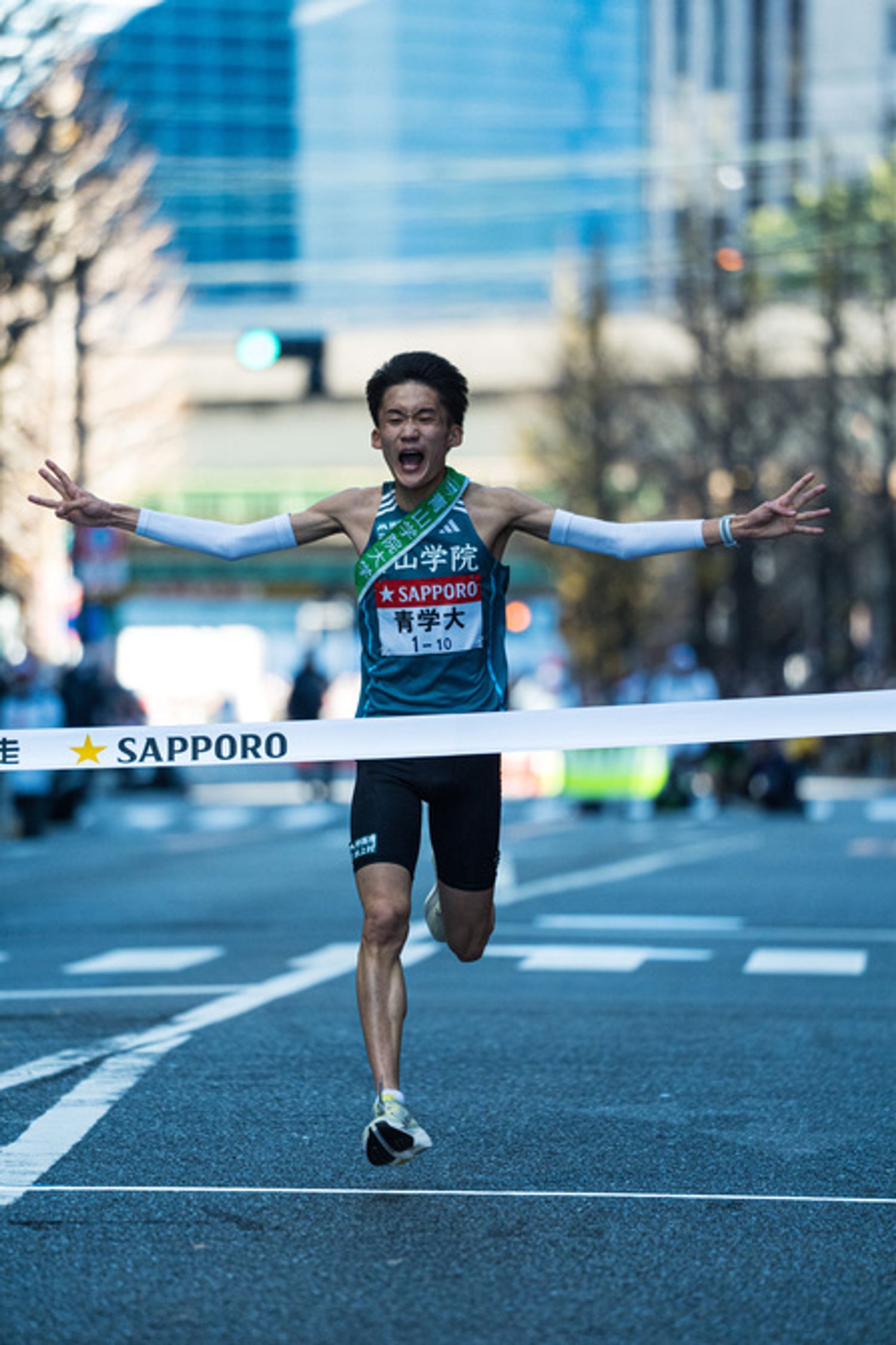 1月3日の大手町、溢れた涙を拭い、笑顔でゴールする折田選手（2年）。右手で3連覇を表し、左手で4連覇への意気込みをアピール。両手の指を合計した７という数字は、亡きチームメイト、皆渡星七選手に捧げられた。世代トップランナーとして入学したものの、1年目は怪我に苦しんだ折田選手。10区で駒澤大学の大エース、佐藤圭汰選手(4年)に次ぐ区間2位のタイムで快走したことで、復活を印象づけた。本領発揮はこれからだ。