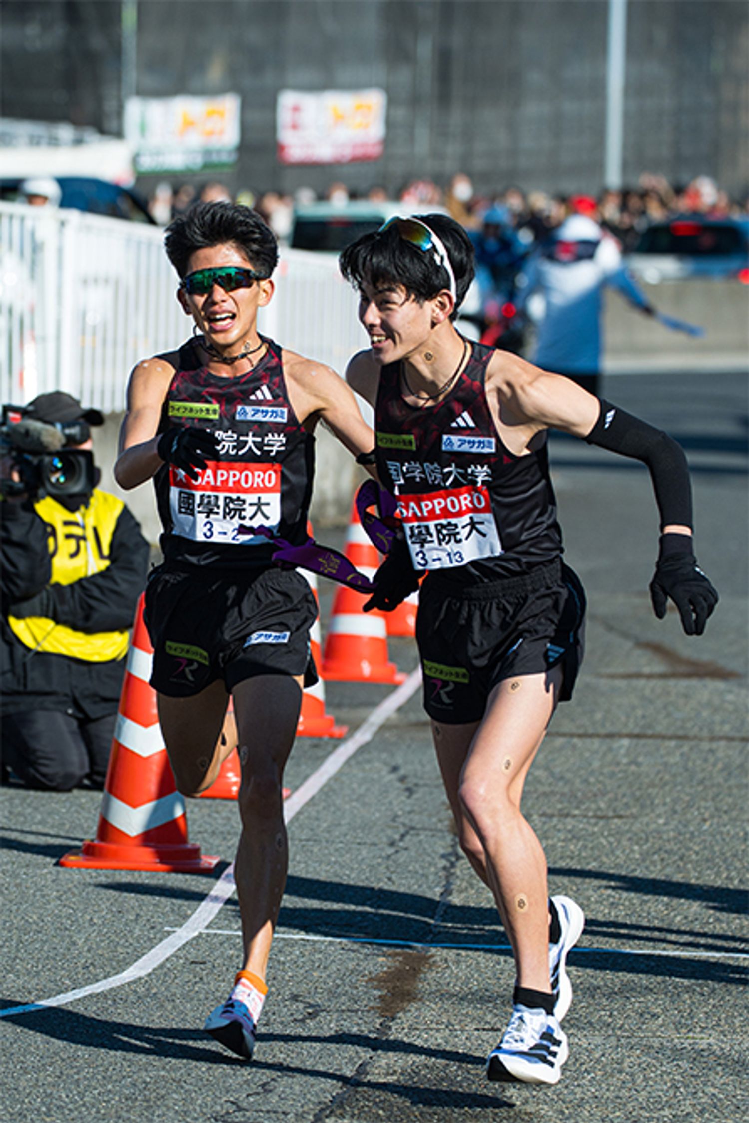 2区上原主将（左・4年）から、3区野中恒亨選手（右・3年）へ襷が渡る。上原主将は各大学の実力者が揃ったエース区間を区間12位で走り、チームの順位は1位から6位へ。頼れるエースの1人、野中選手は区間3位のタイムで順位を1つ上げ、5位で辻原 輝選手（3年）に襷を繋いだ。