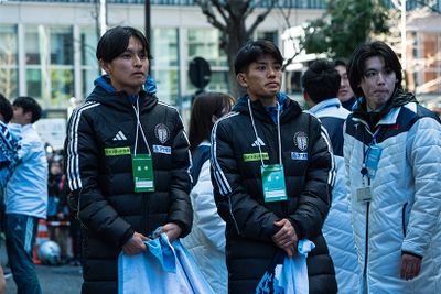 大手町のゴールエリアで、大会運営スタッフ（右端）とともに尾熊迅斗選手（2年）の到着を待つ青木瑠郁副将（左・4年・1区）と上原琉翔主将（中央・4年・2区）。箱根駅伝では優勝校以外、ゴールでアンカーを迎えられるのは各大学２名まで。準優勝校も例外ではない。すぐ後ろで青山学院大学が歓喜の胴上げを行うなか、今季のチームを牽引した4年生２人は口を真一文字に結んで前だけを見ていたが、視界に尾熊選手を捉えると一変、「尾熊！」「ラストー！」と声を張り上げた。