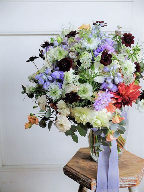 ピンク系の贈り花の引き締め役によくチョコレートコスモスを利用しますが、これは白とブルーの花色合わせに使ったもの。深く落ち着いた花色がパッと目立ち、ブーケが個性的な印象になりました。デルフィニウム‘トリトン ラベンダー’、ラナンキュラスの‘ポンポンイグルー’、‘ラックス ニノス’、‘ラックス エリス’、スカビオサの‘プチポンポン ホワイト’と‘ナナラベンダー’、ダリア‘NAMAHAGE オーブ’、バラ‘グリーンアイス’、ニゲラ‘ミスジーキル’、アストランティア・マヨール、ユーカリなど、種類豊富に集めました。