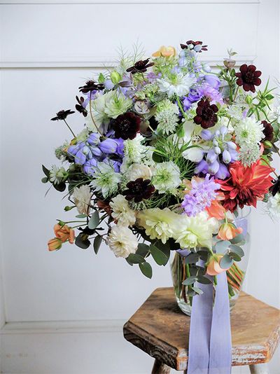 ピンク系の贈り花の引き締め役によくチョコレートコスモスを利用しますが、これは白とブルーの花色合わせに使ったもの。深く落ち着いた花色がパッと目立ち、ブーケが個性的な印象になりました。デルフィニウム‘トリトン ラベンダー’、ラナンキュラスの‘ポンポンイグルー’、‘ラックス ニノス’、‘ラックス エリス’、スカビオサの‘プチポンポン ホワイト’と‘ナナラベンダー’、ダリア‘NAMAHAGE オーブ’、バラ‘グリーンアイス’、ニゲラ‘ミスジーキル’、アストランティア・マヨール、ユーカリなど、種類豊富に集めました。