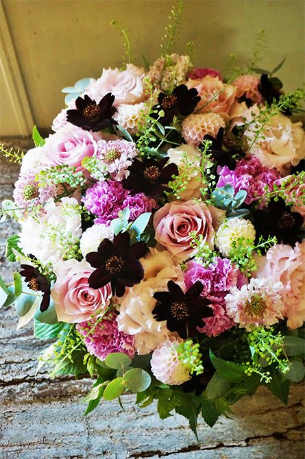 お母様へ、感謝の気持ちを込めたフラワーバレンタインの贈り花です。バラ、リシアンサス、カーネーション、マイクロポンポンダリアと、ボリューム感ある花をギュッと詰めてアレンジに。チョコレートコスモスを間に加えると、凹凸感からメリハリが生まれます。バラは‘リメンブランス’、リシアンサスは‘NF秋ピンク’、カーネーションは‘シャララ ライト’をセレクト。ほかにスカビオサ‘ベビーピンク’、タラスピオファリム、ダスティーミラー、ユーカリなどを使用。